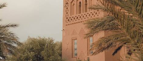 A traditional building with intricate lattice work and arched windows, surrounded by lush greenery.