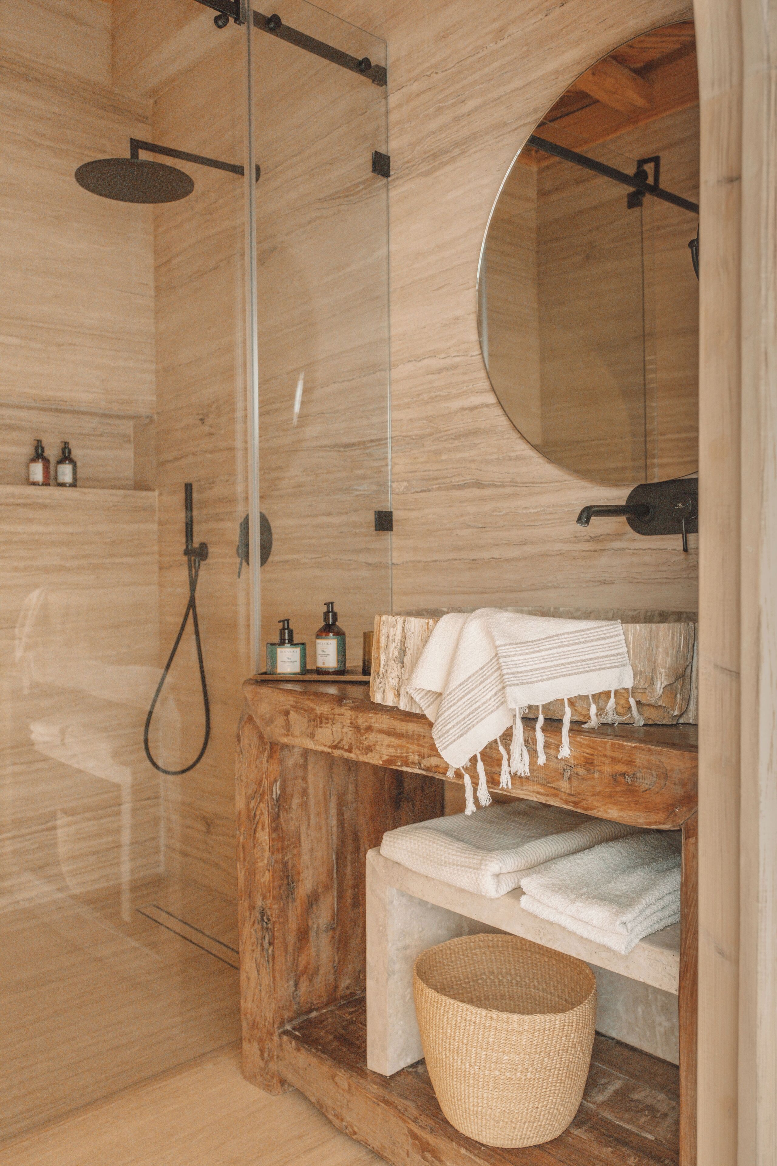 Un baño de madera con ducha envuelta en vidrio, tocador de madera con espejo y toallas dobladas con cuidado.