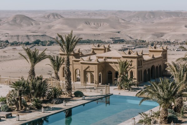A desert resort with a swimming pool, palm trees, and a view of the desert landscape.