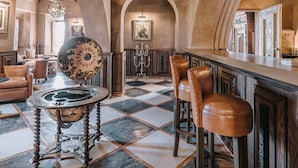 Un espace bar doté d’un plafond haut, de poutres en bois et d’un lustre. On y trouve des tabourets de bar et une table ronde avec un plateau décoratif.