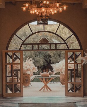 An arched doorway with frosted glass panels, leading to a garden area with a central table and potted plants. - KASBAH D'IF (Tameslouht)