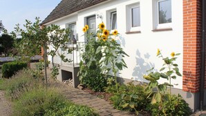 Ein weißes Haus mit Ziegelanbau, einem Balkon und Sonnenblumen im Garten.