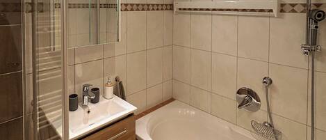 Ein Badezimmer mit Duschkabine aus Glas, einer Badewanne, einem Waschtisch mit Spiegel und einem Handtuchhalter.