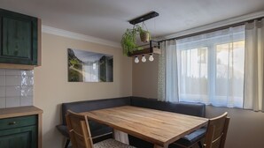 Une cuisine avec une table en bois, deux chaises, un banc et une plante suspendue.