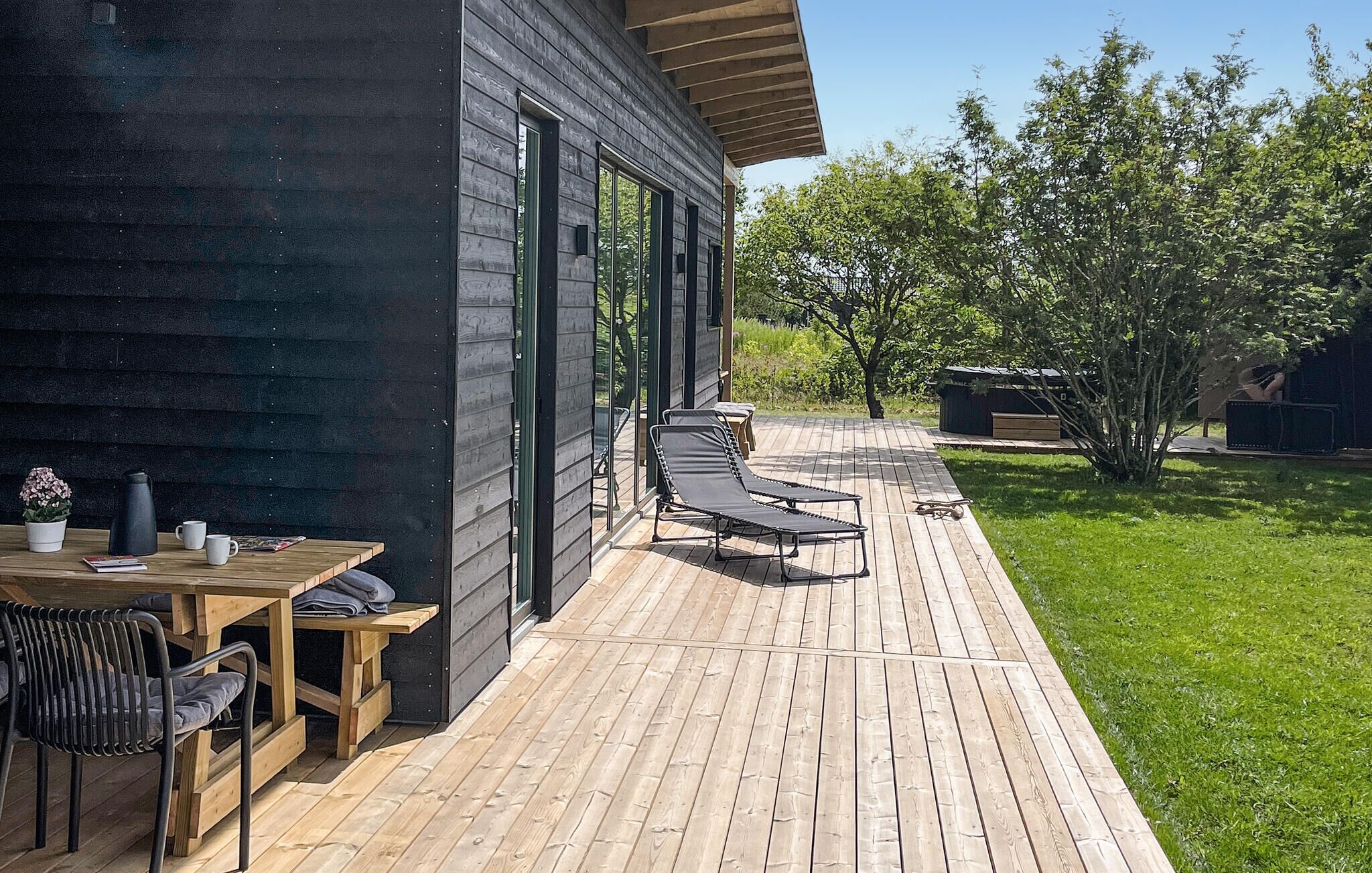 A wooden deck with a table and chairs, a small garden area, and a building with large windows.