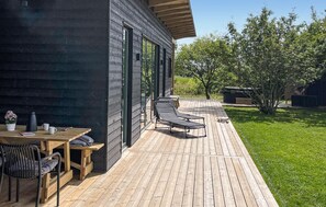 A wooden deck with a table and chairs, a small garden area, and a building with large windows. - Gorgeous home in Tarm with sauna (Tarm)