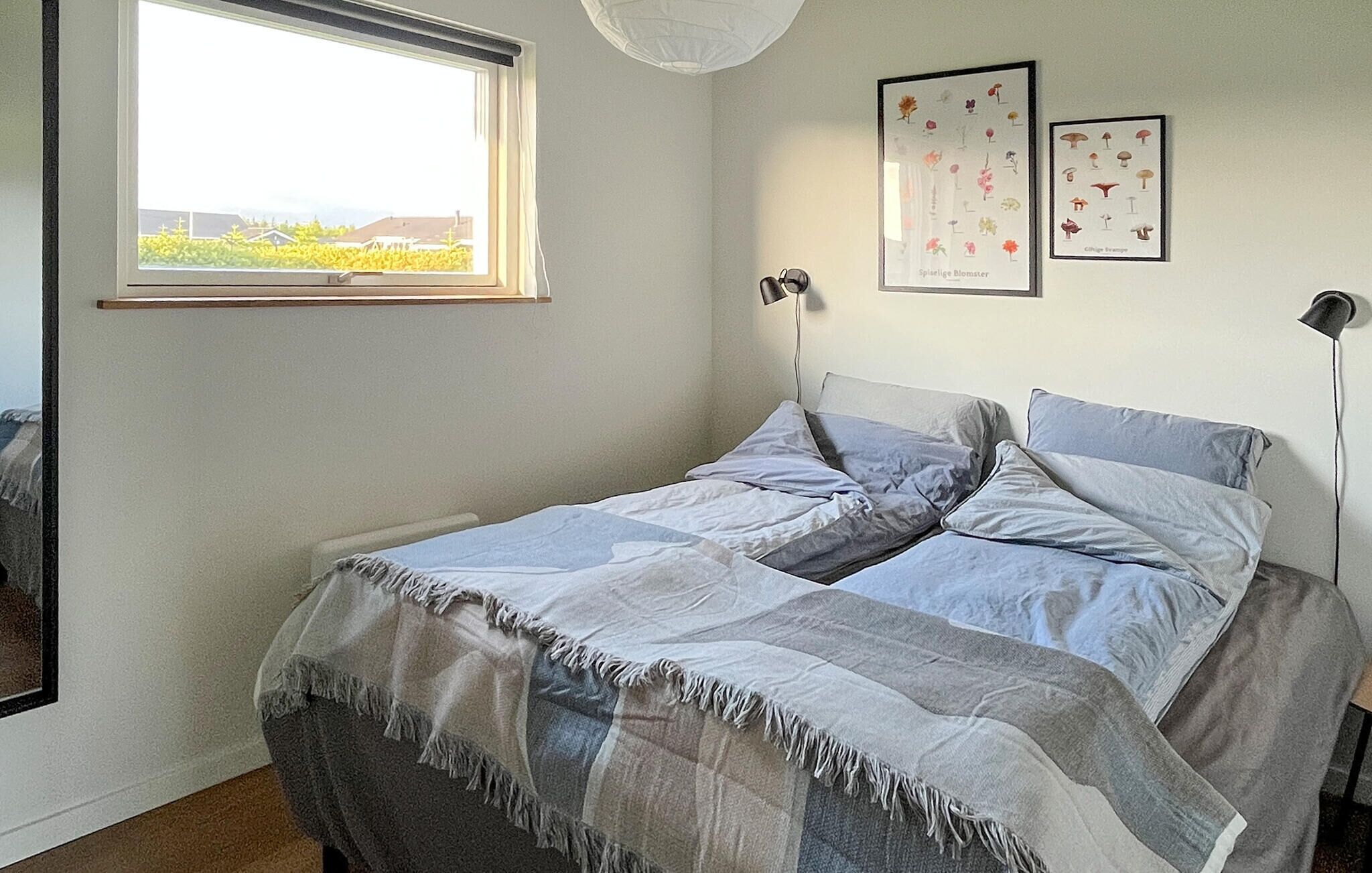 Une chambre à coucher avec un lit, une fenêtre et deux reproductions botaniques encadrées accrochées au mur.
