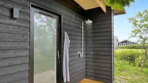 Ein moderner, überdachter Duschenbereich im Freien mit Holzboden, Glastür und Handtuch an der Wand.