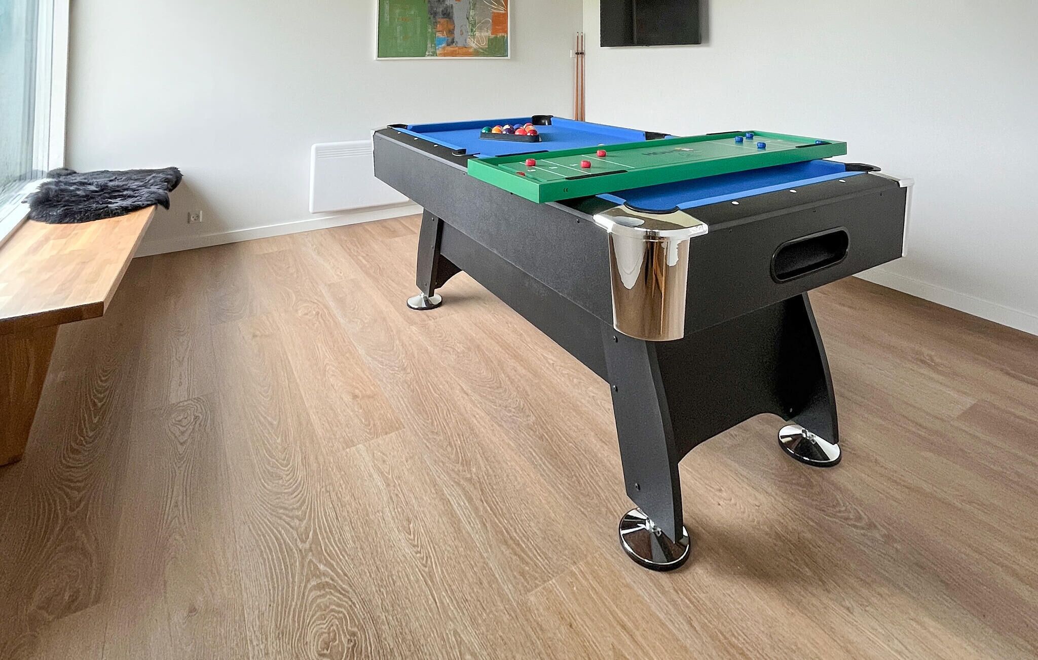 A foosball table in a room with wooden flooring and a bench.