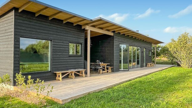 Eine moderne Blockhütte mit Terrasse, großen Fenstern und Sitzgelegenheit im Freien.