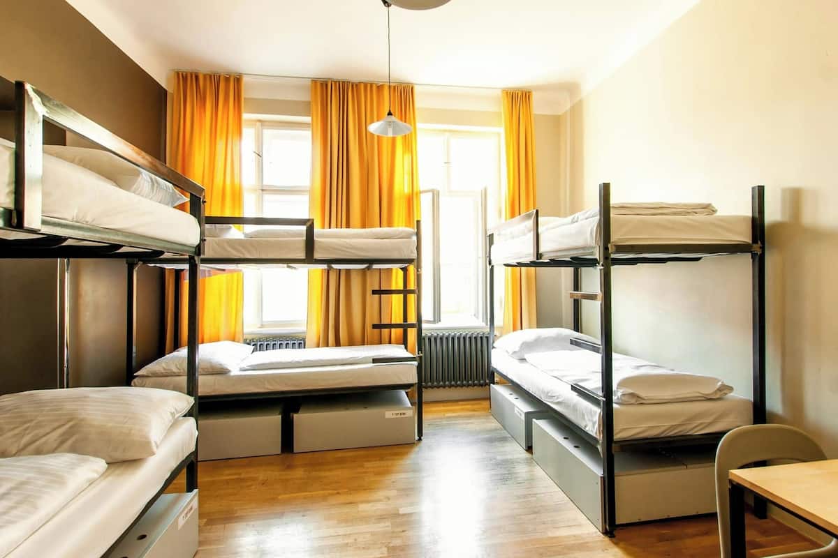 A dormitory room with bunk beds, a desk, and a window with curtains.