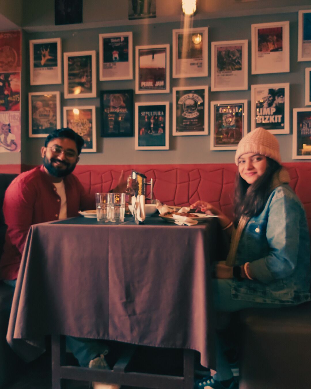A restaurant with a red cushioned bench seating, a table with a purple tablecloth, and various framed posters on the wall.