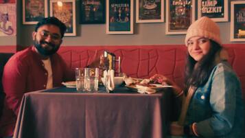 A restaurant with a red cushioned bench seating, a table with a purple tablecloth, and various framed posters on the wall.
