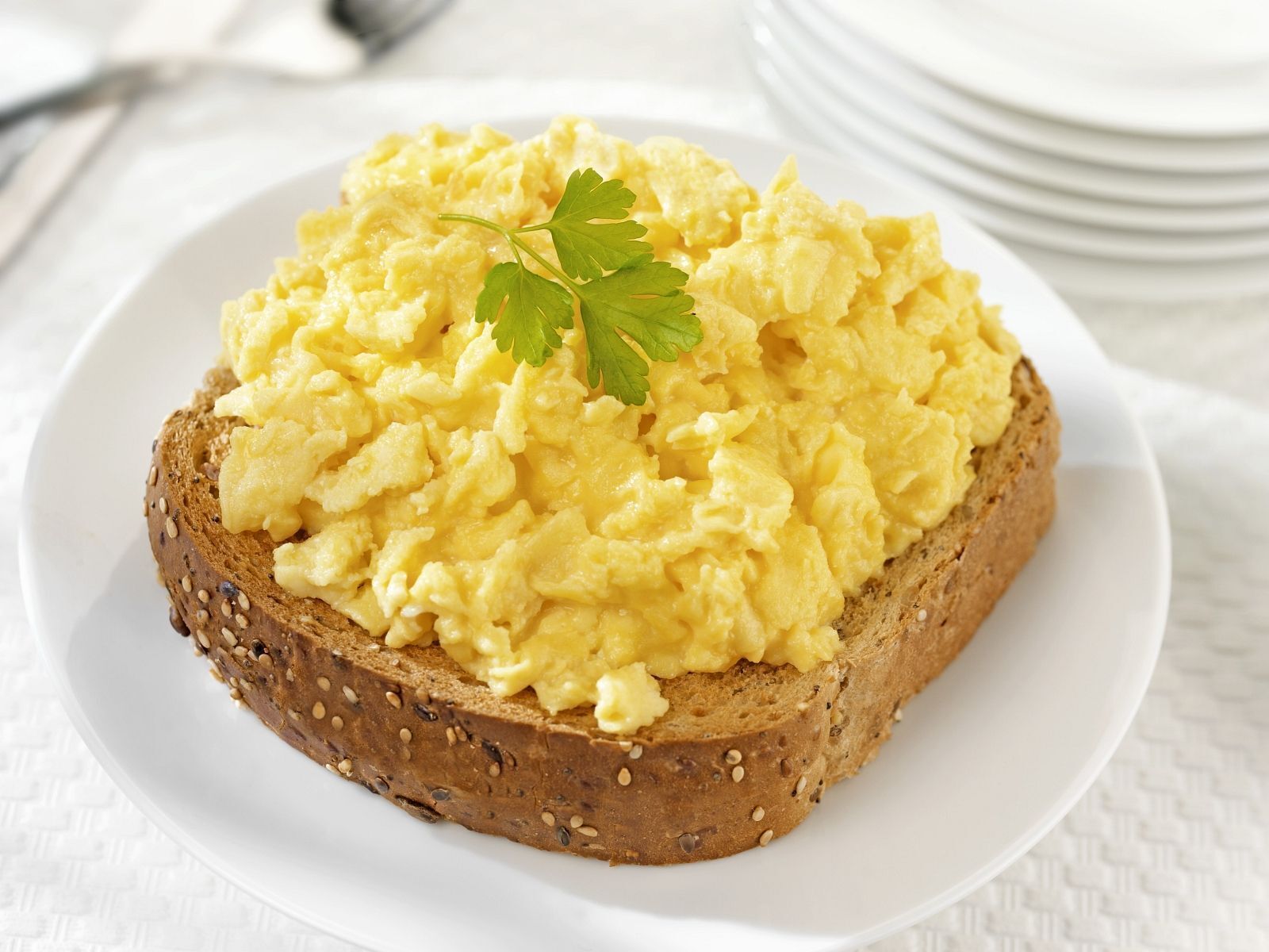 Una tostada con huevos revueltos y una ramita de perejil sobre un plato blanco.