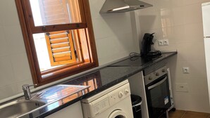 Une cuisine compacte équipée d’un lave-linge et d’un sèche-linge intégrés, d’une cuisinière et d’une fenêtre avec des stores.