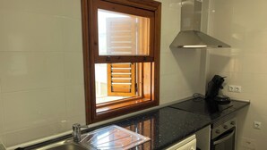 Une cuisine de taille réduite comprenant un évier, une fenêtre avec stores, une cuisinière et un lave-linge.