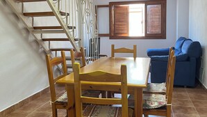 Un espace repas avec une table et des chaises en bois, un escalier avec des rampes en métal, un ventilateur de plafond et une fenêtre avec des stores.