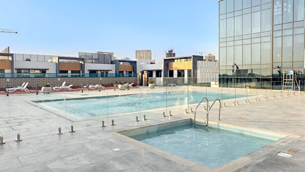 Ein Poolbereich auf dem Dach mit zwei Pools, Liegestühlen und einem modernen Gebäude im Hintergrund.
