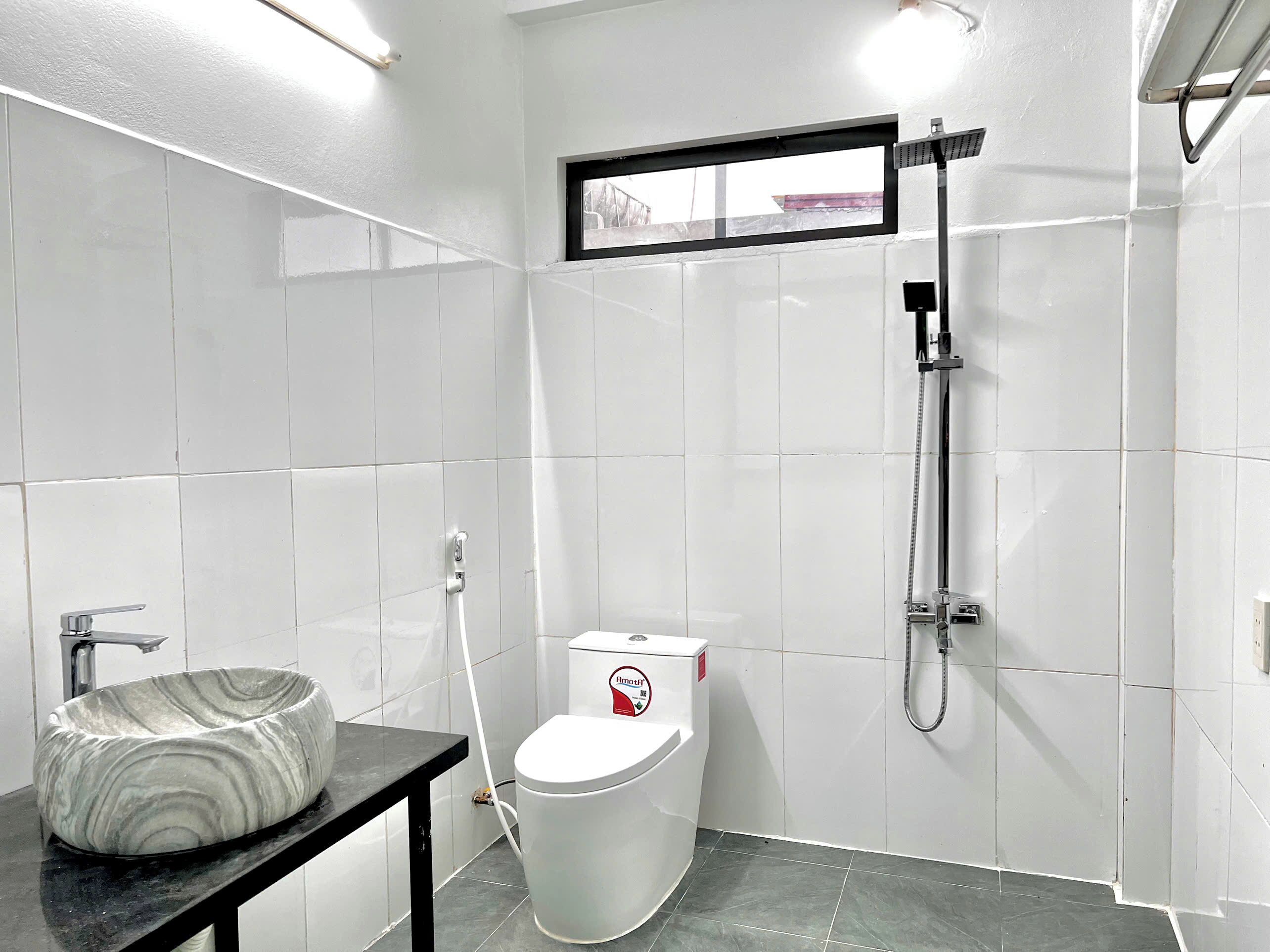 A modern bathroom with white tiles, a marble sink, a toilet, and a shower.