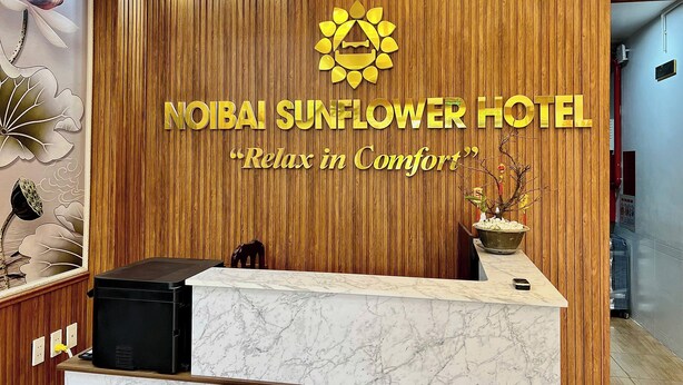 A reception desk with a wooden panel wall, a logo, and the text "NOBAI SUNFLOWER HOTEL" and "Relax in Comfort". - Noibai Sunflower Hotel (Hanoi)