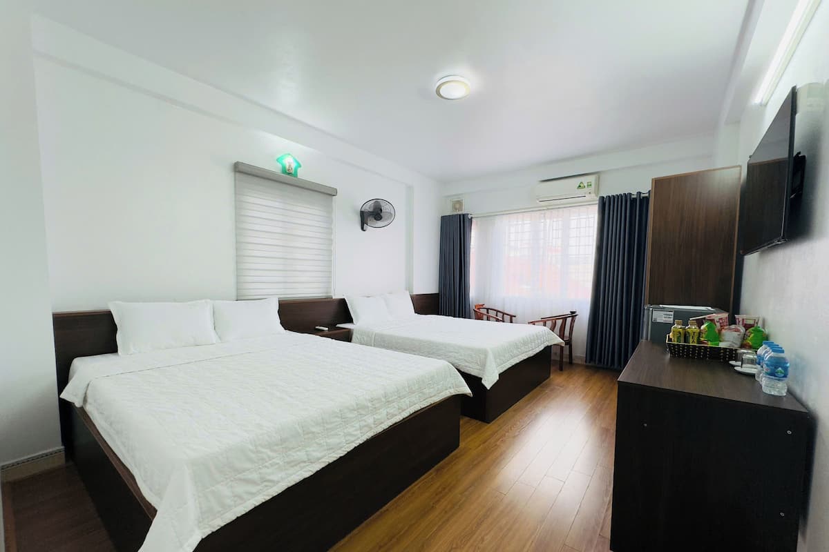 Une chambre d’hôtel avec deux lits, un bureau avec des articles de toilette, une télévision et une fenêtre avec des rideaux.