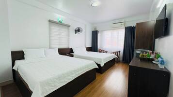 A hotel room with two beds, a desk with toiletries, a TV, and a window with curtains.