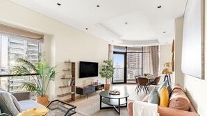 A modern living room with a flat-screen TV, a dining area with a table and chairs, and a sofa.