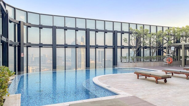 An infinity pool with a glass barrier, lounge chairs, and a city view.