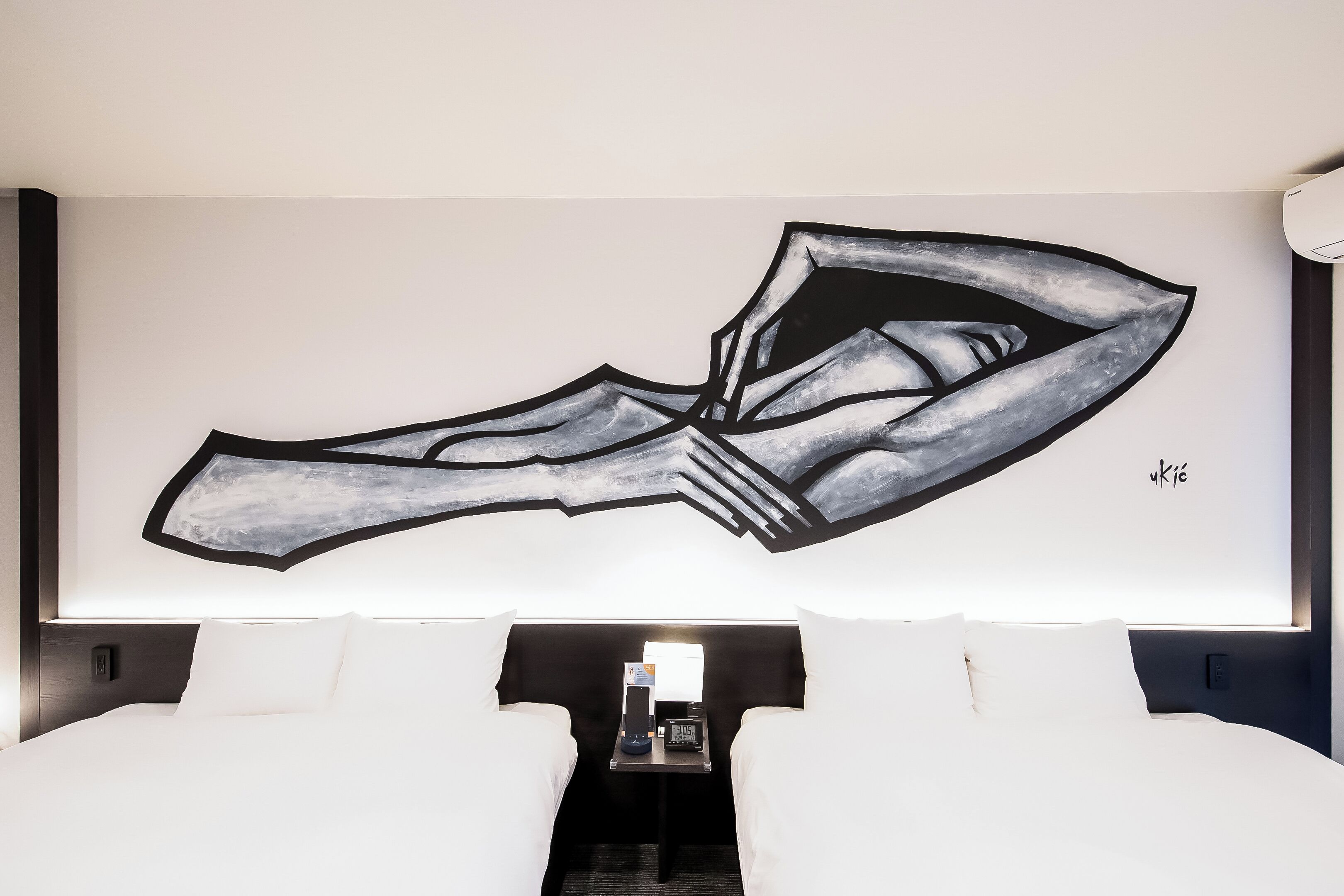 Una habitación de hotel con una cama grande, una mesita de noche con un reloj y una obra de arte en la pared.