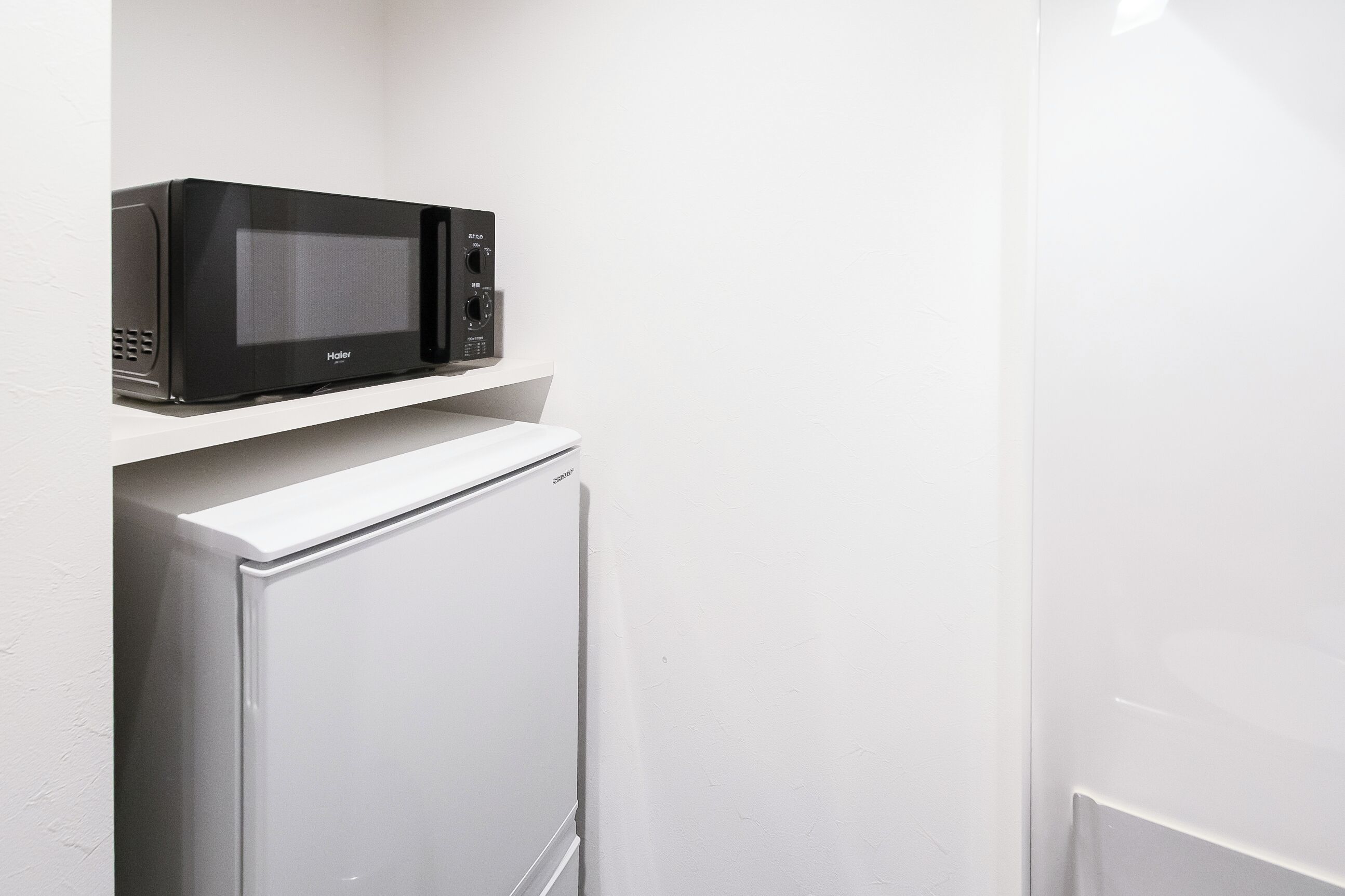 Una cocina compacta con un microondas negro sobre un estante blanco, encima de un refrigerador blanco.