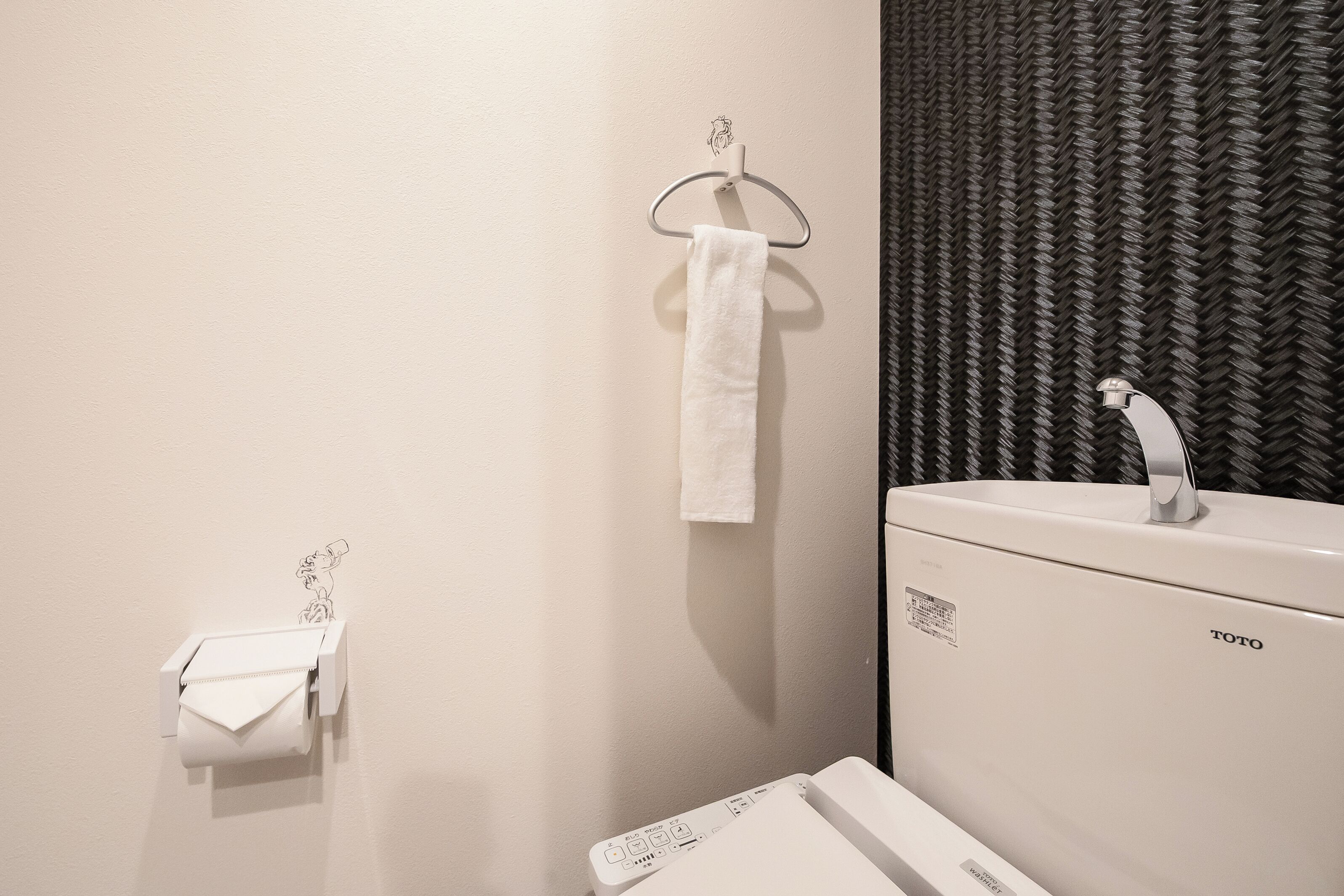 Un baño con un lavamanos blanco, una toalla colgada en un aro metálico y un dispensador de papel higiénico.