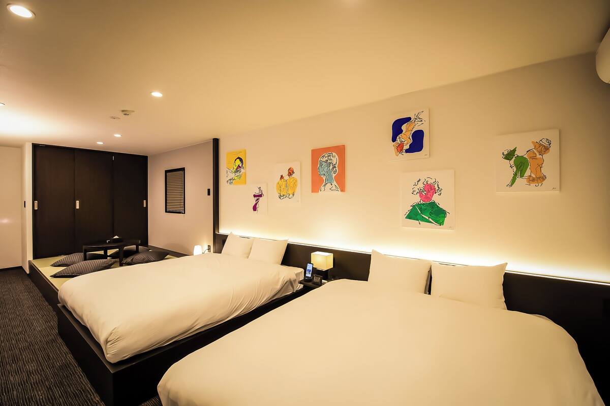 Habitación de hotel con dos camas, un escritorio y obras de arte en las paredes.