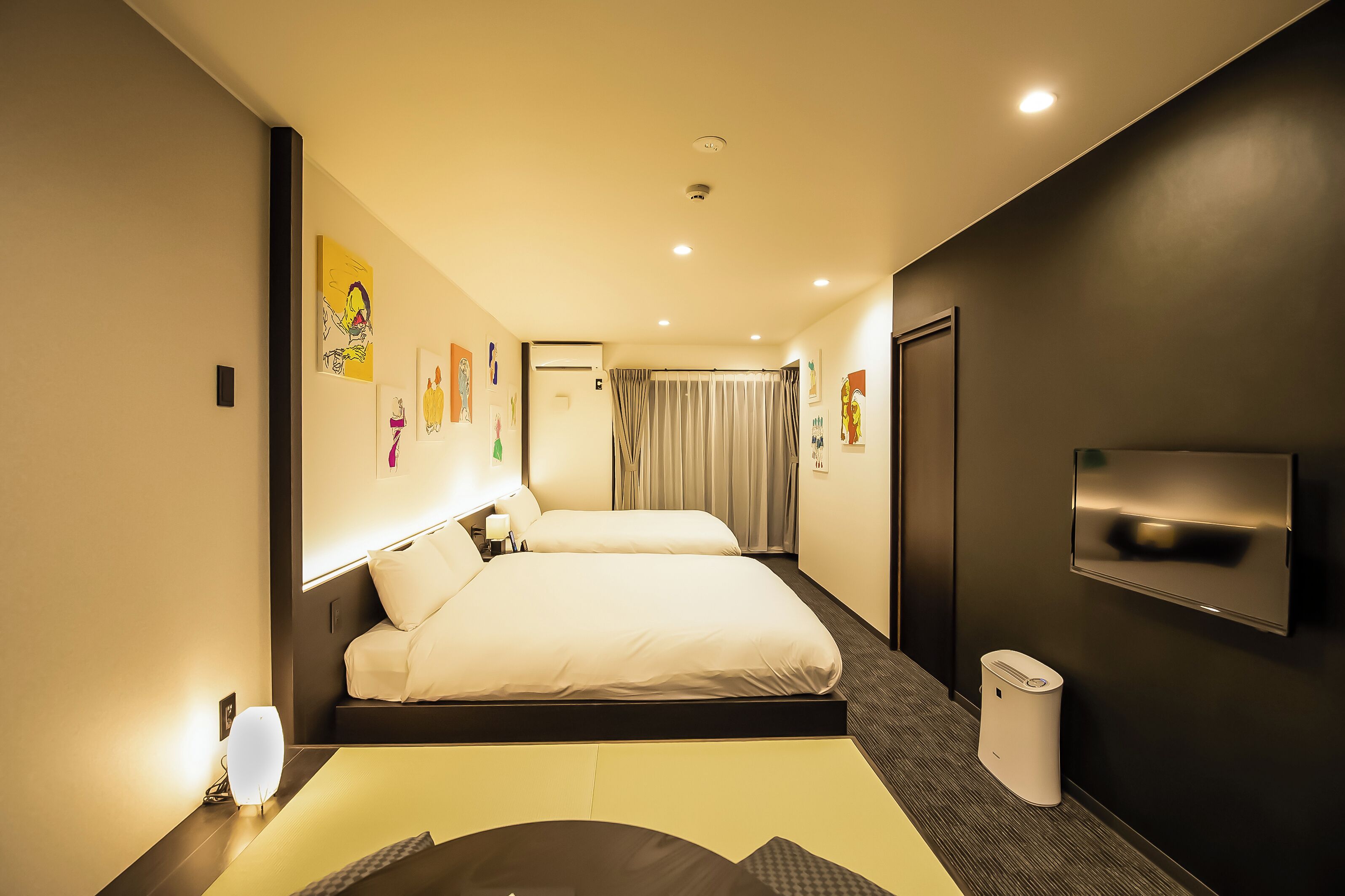 Una habitación de hotel moderna con una cama grande, mesitas de noche, un televisor y obras de arte en las paredes.