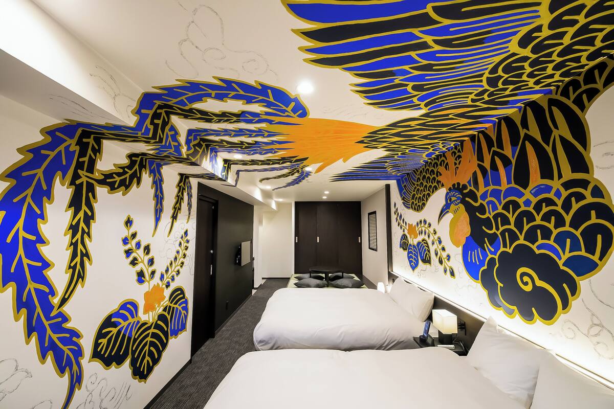 Una habitación de hotel con una cama grande, una cama más pequeña y un escritorio con una lámpara.