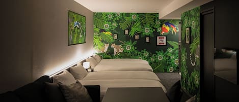 Habitación de hotel con una cama, un sofá, un escritorio y una pared decorada con un mural de temática selvática.