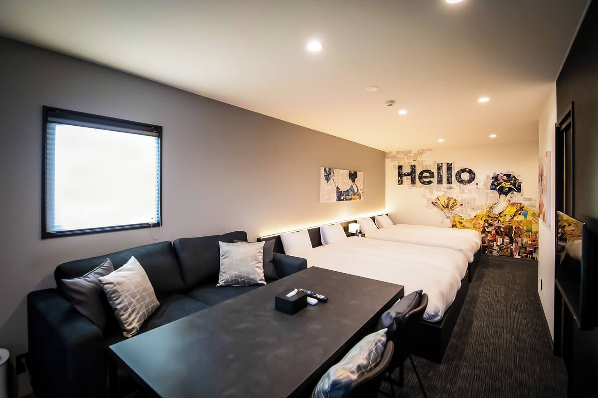 Una habitación de hotel moderna con sofá, cama, mesa y una decoración de pared que dice 'Hello'.
