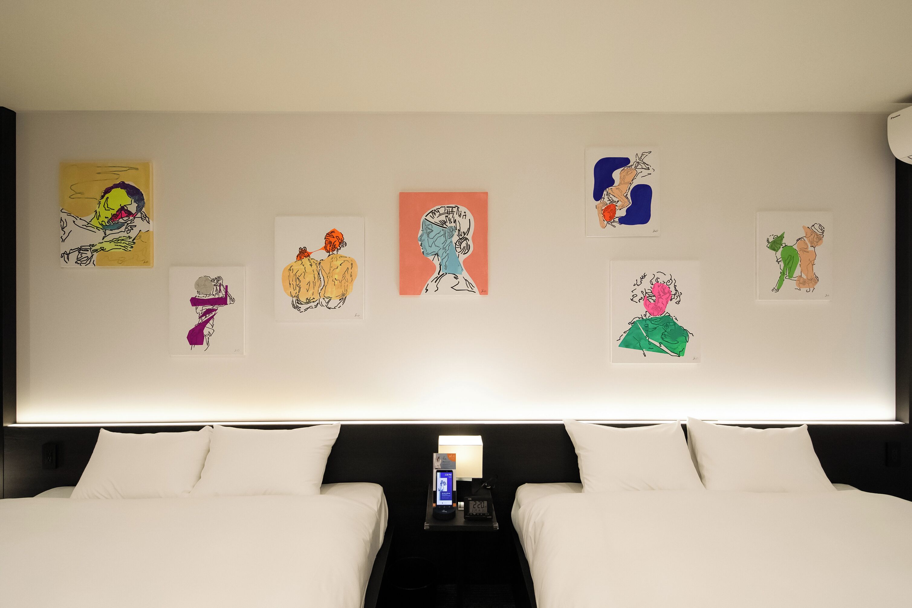A hotel room with a large bed, a bedside table with a lamp, and multiple artworks on the wall.