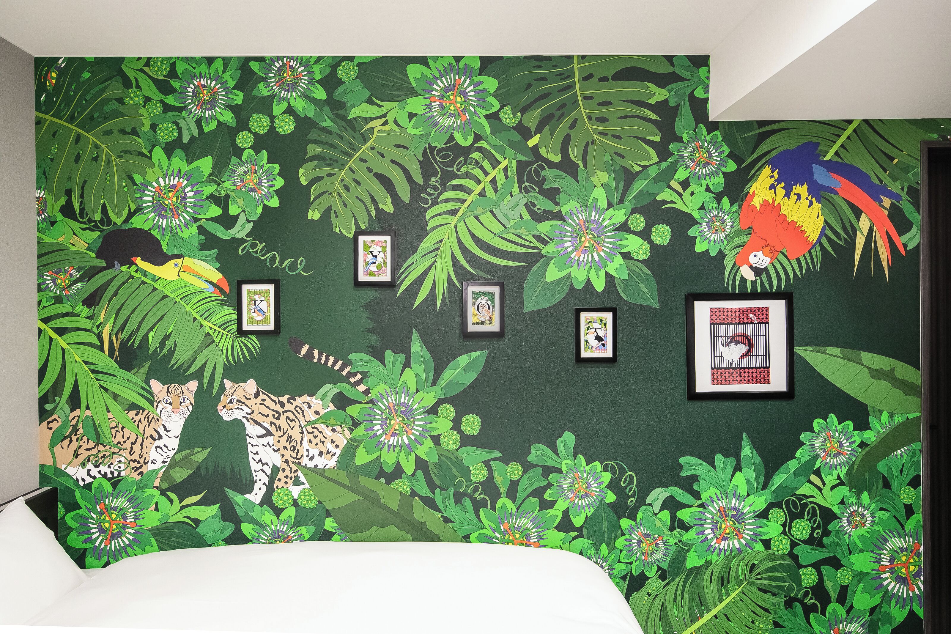 A room with a green wall featuring a jungle-themed mural, a bed, and several framed pictures.