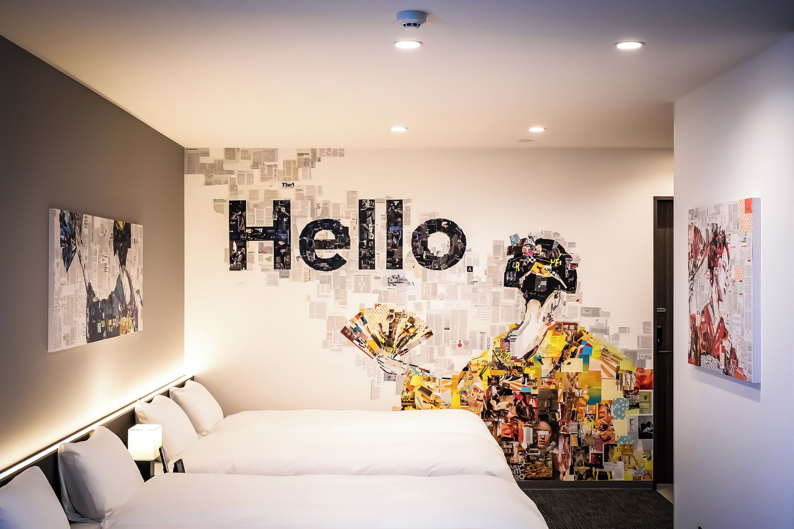 A modern hotel room with a large bed, a wall art installation, and a "Hello" sign.