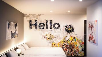 A modern hotel room with a large bed, a wall art installation, and a "Hello" sign.
