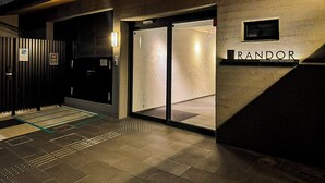 Una entrada de hotel moderna con una puerta de cristal, una placa con el nombre "RANDOR" y una rampa que conduce a la entrada.