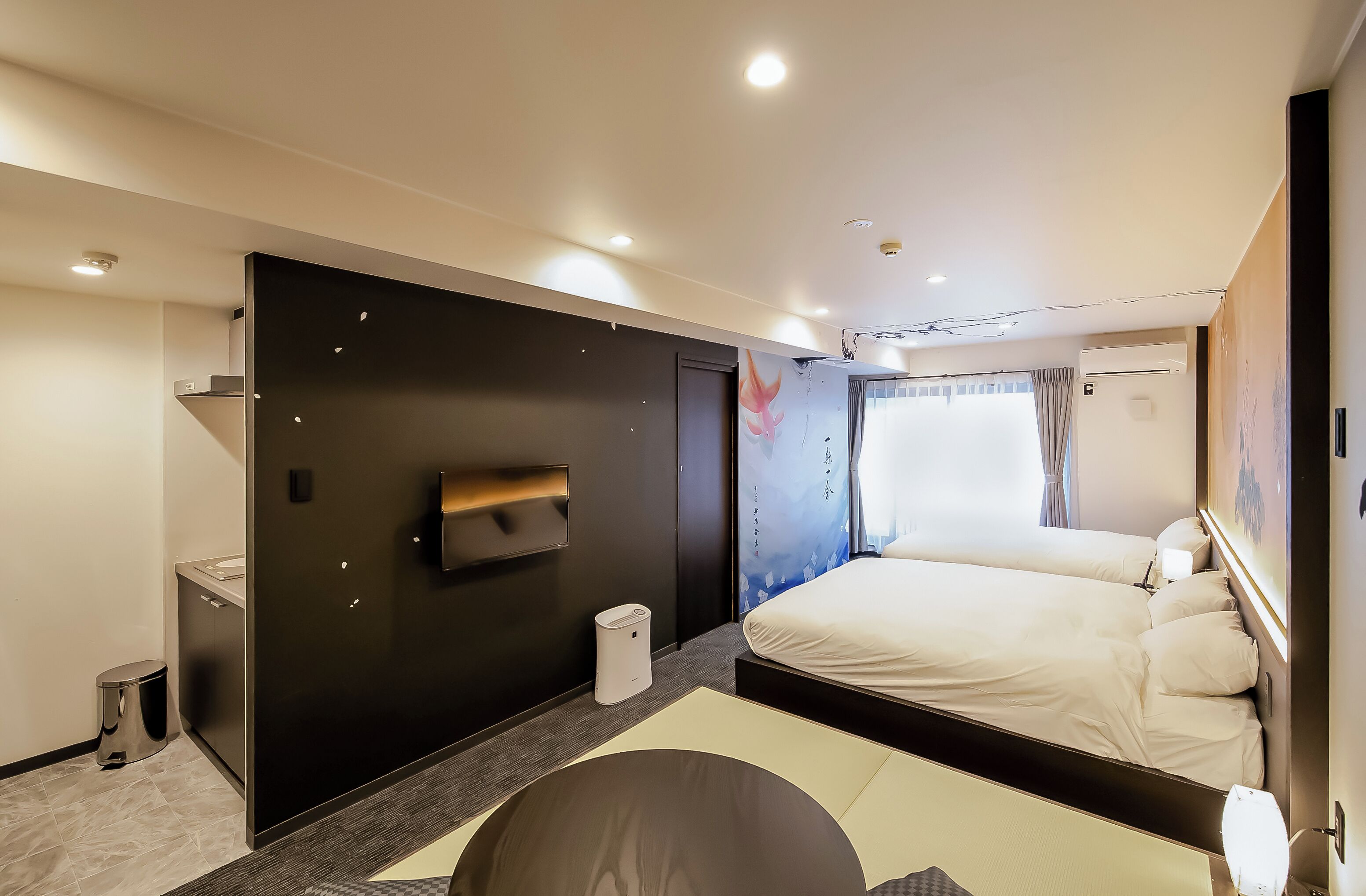A modern hotel room with a large bed, a flat-screen TV mounted on the wall, a small bedside table, and a window with curtains.