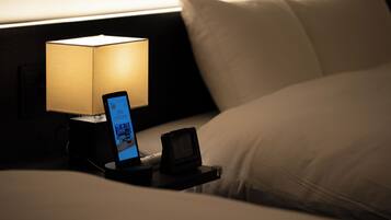 A neatly made bed with white sheets and pillows, a bedside table with a lamp, and a smartphone displaying a VR app.