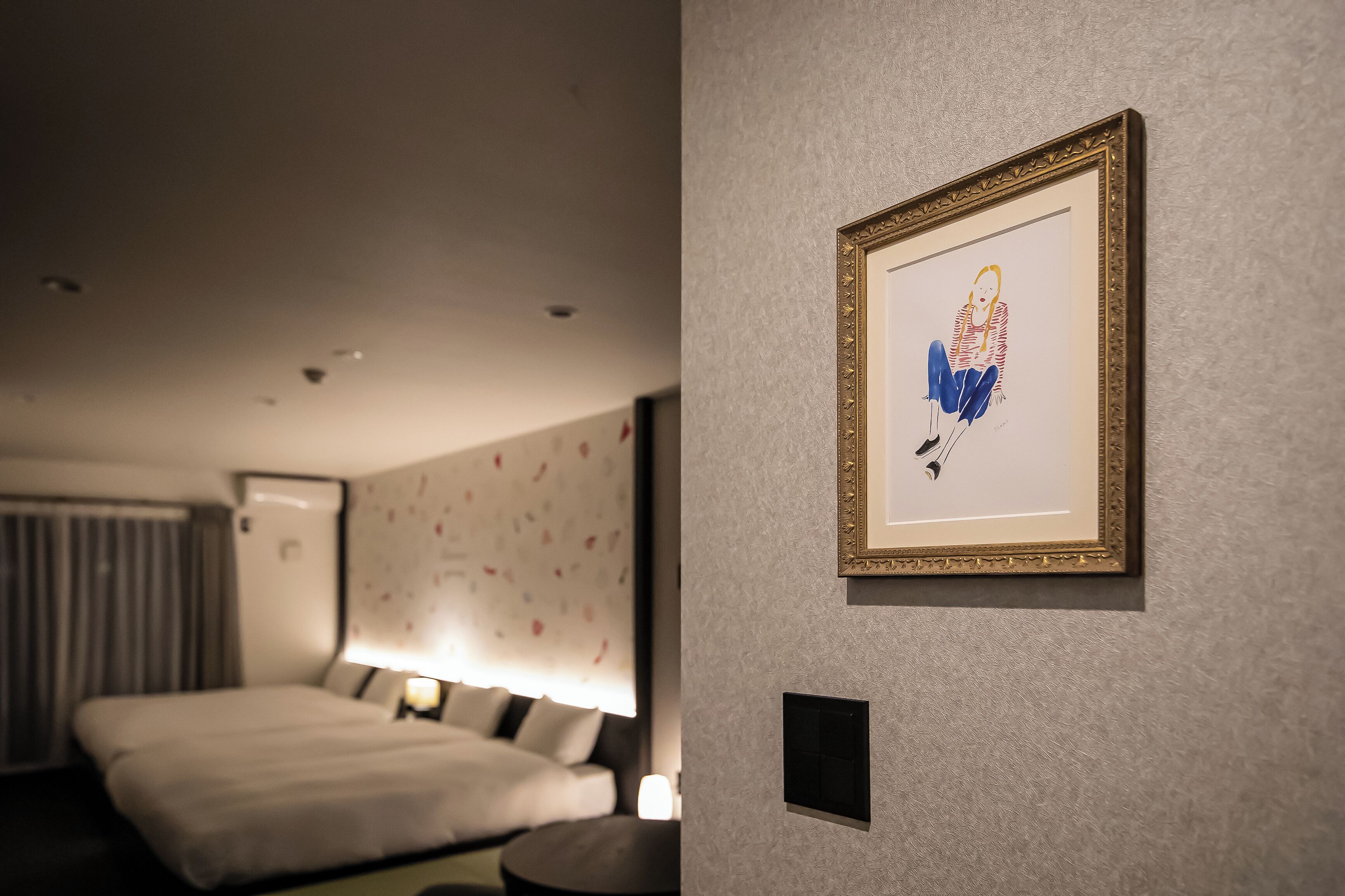 Ein Hotelzimmer mit einem Bett, einem Nachttisch, einer Wand-Klimaanlage und einem gerahmten Kunstwerk an der Wand.