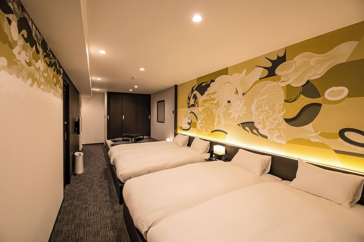 Habitación de hotel con tres camas, un gran mural decorativo y una pequeña zona de escritorio.