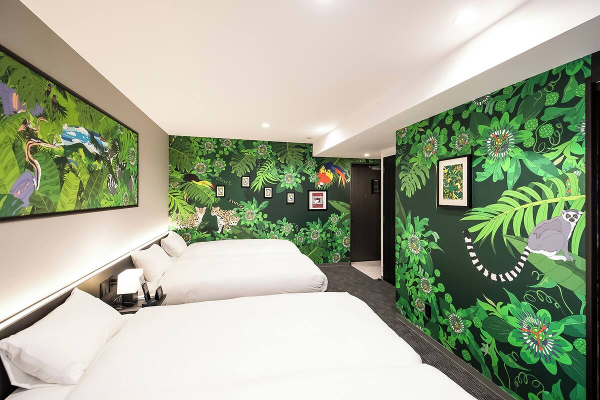 Habitación de hotel con dos camas, papel tapiz floral verde, cuadros en las paredes y un cuadro grande sobre las camas.