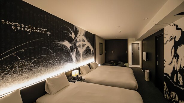 Habitación de hotel con dos camas, un cuadro abstracto grande en la pared y una puerta que da a otra habitación.