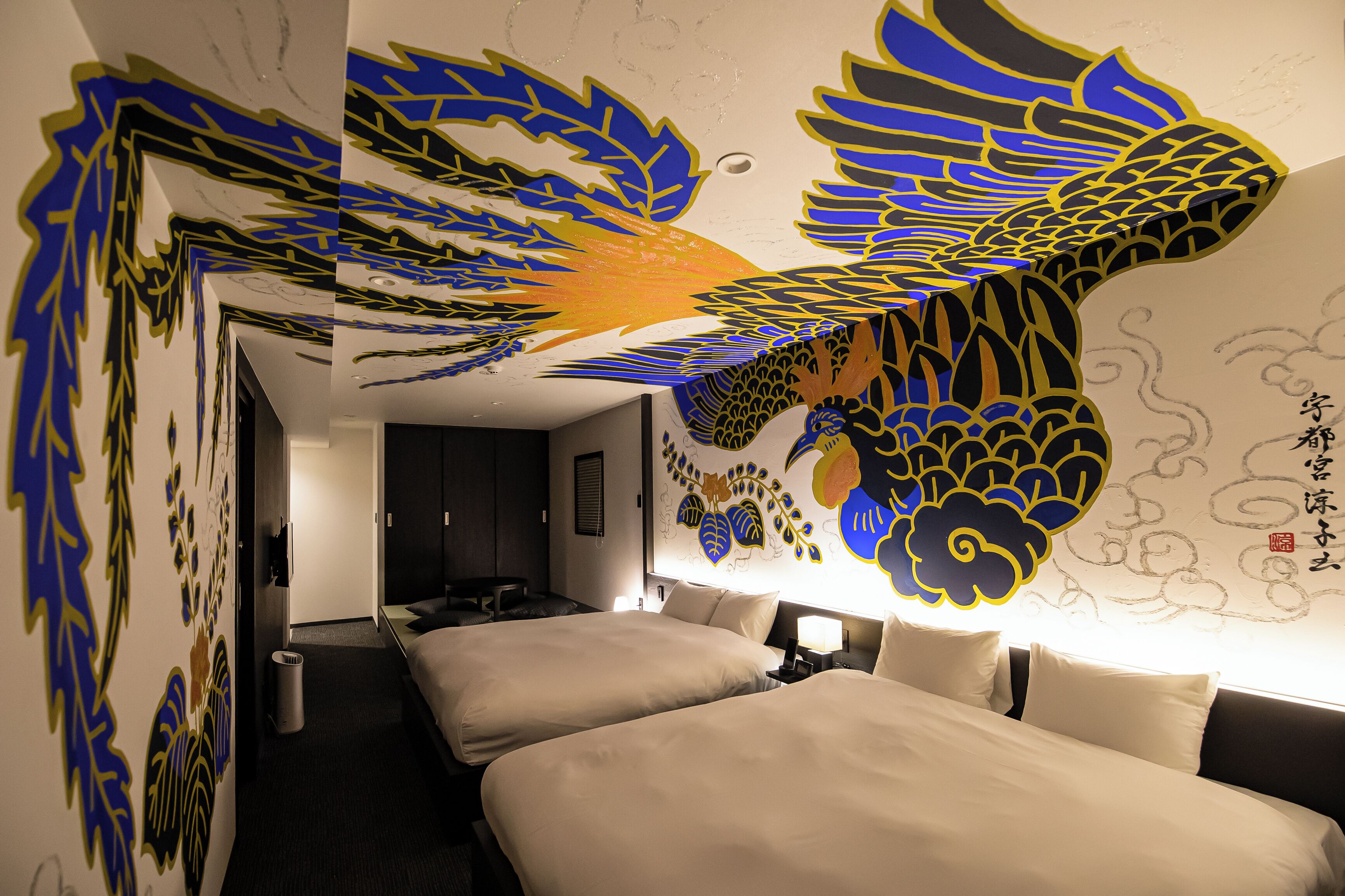 A hotel room with a large decorative wall mural, a bed, a bedside table, and a nightstand.