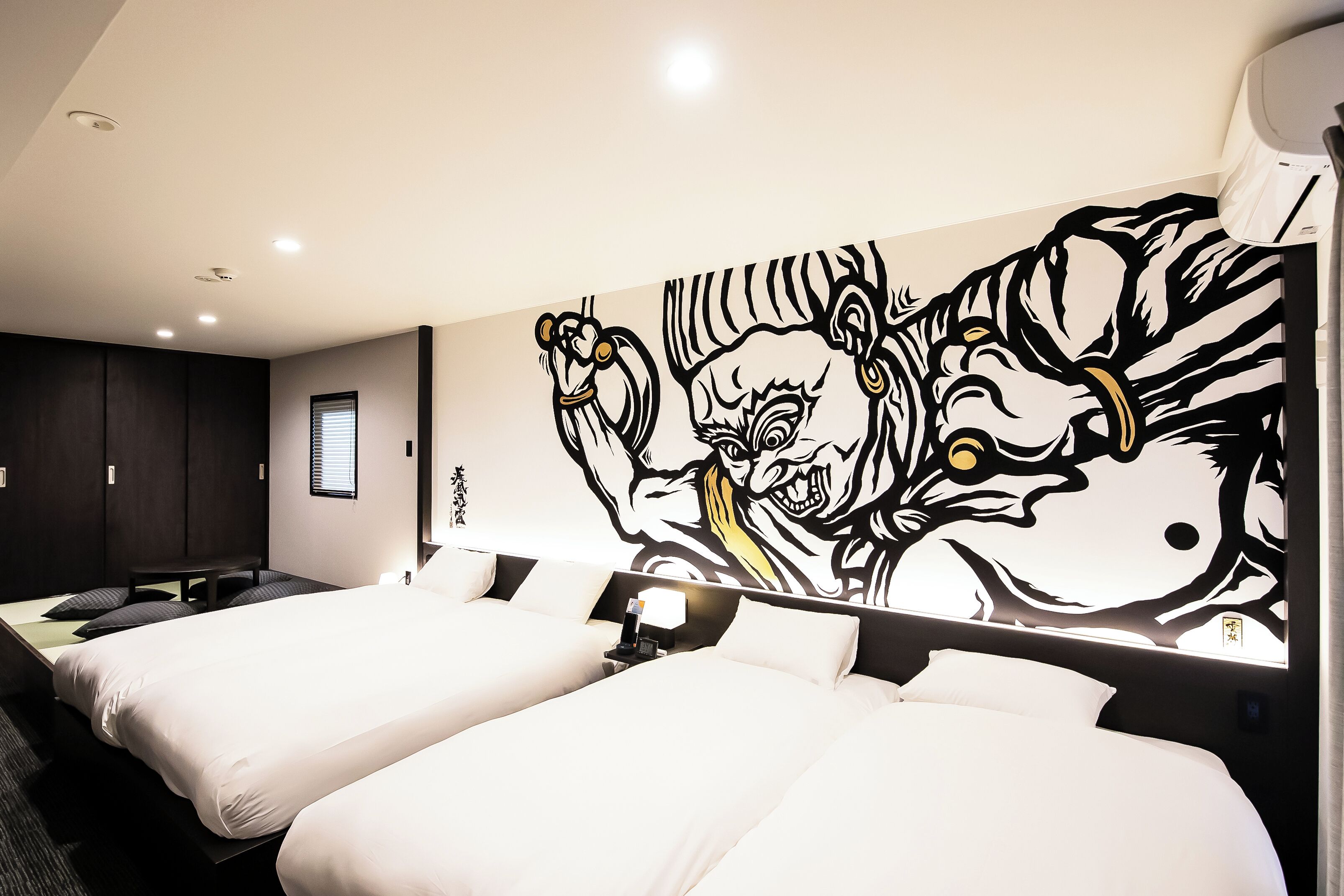 Une chambre d’hôtel avec deux lits, une grande fresque murale et une fenêtre avec des stores.