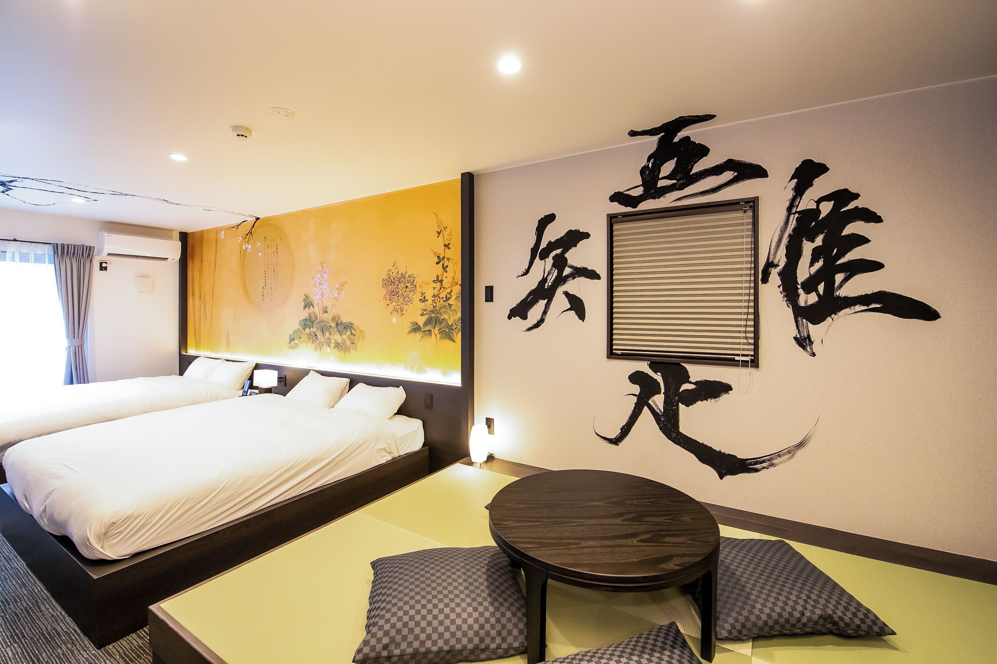 A hotel room with two beds, a round table, and a wall with calligraphy.